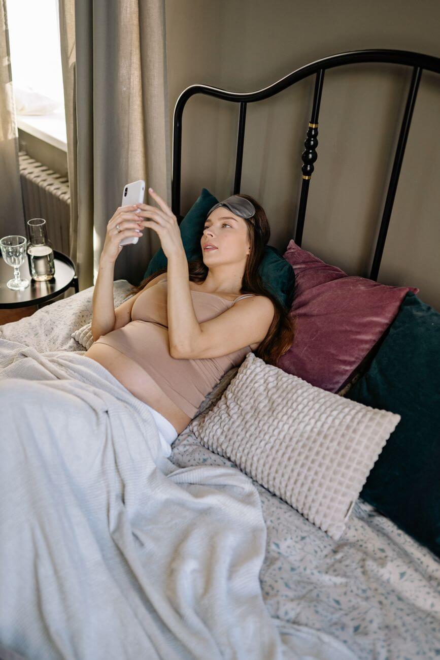 pregnant woman lying on the bed while busy browsing her cellphone