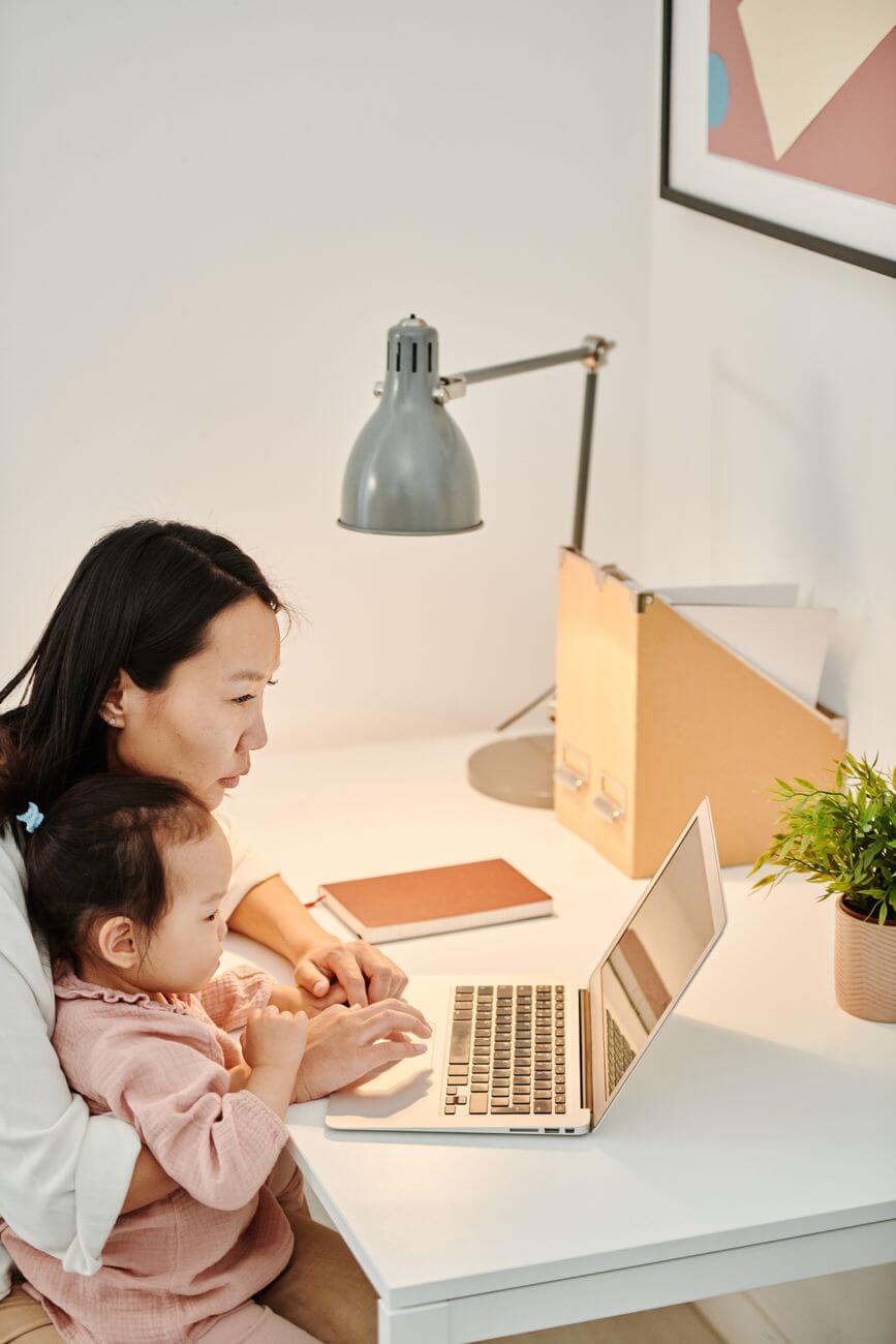 mom using a laptop while taking care of her daughter