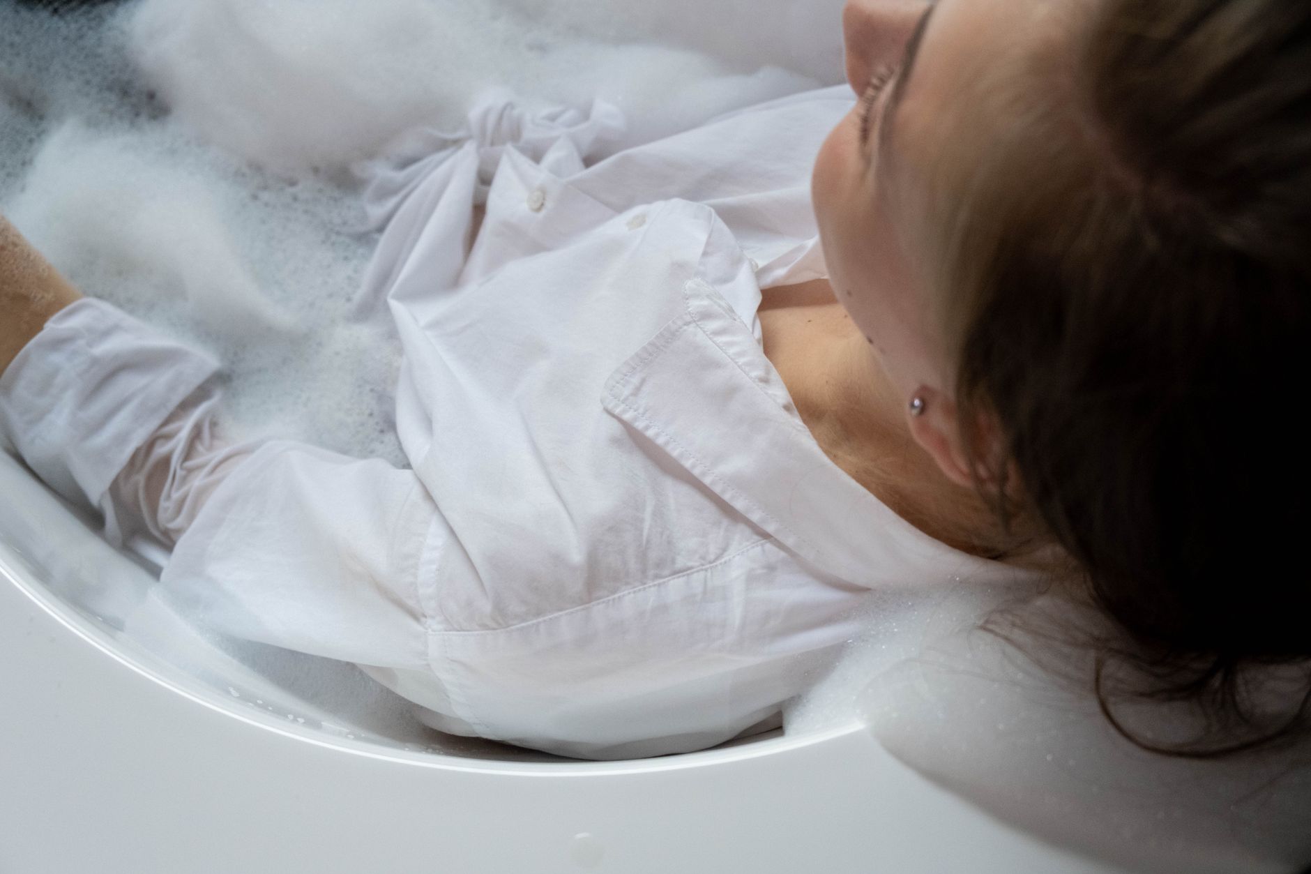 woman in white button up long sleeves resting on a bathtub with water
