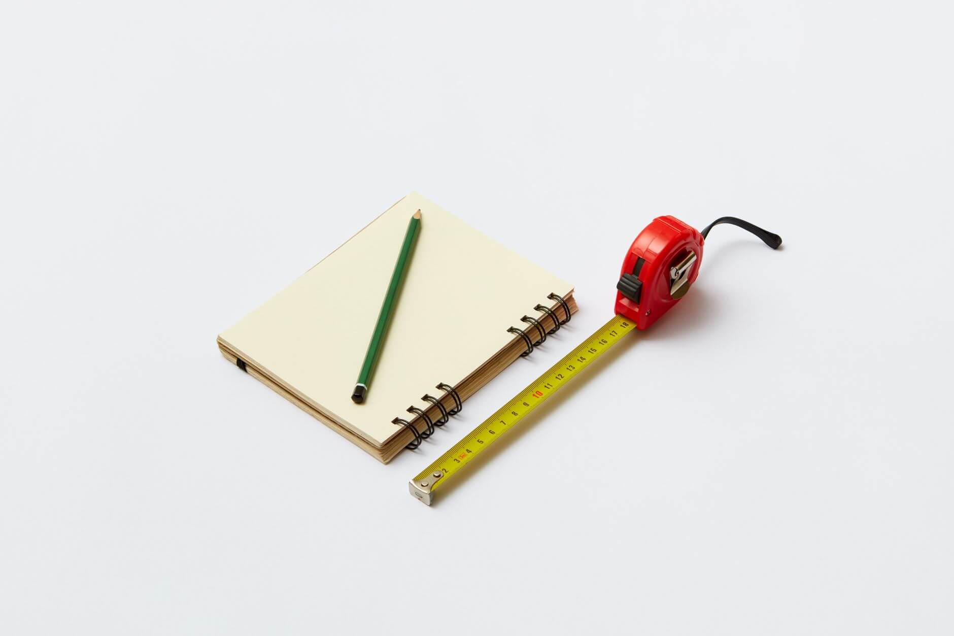 a pencil on a notebook beside a steel blade measuring tape